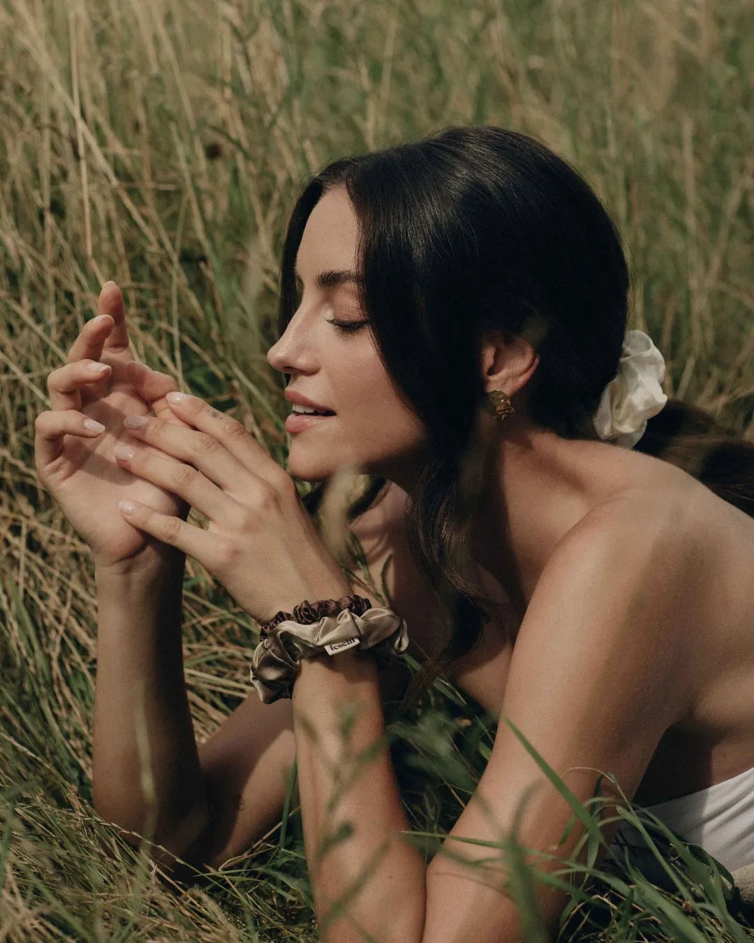 Frau liegt mit dem Bauch auf der Wiese, stützt sich ab und trägt an den Handgelenken die feschi The Silk Edit Seidenscrunchies