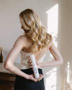 Frau präsentiert den smooth & shine Anti Frizz Spray hinter ihrem Rücken und zeigt ihr glänzendes, blondes Haar. Weniger Frizz, maximaler Glanz