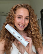 Lächelnde Frau hält das Anti Frizz Spray von feschi in der Hand