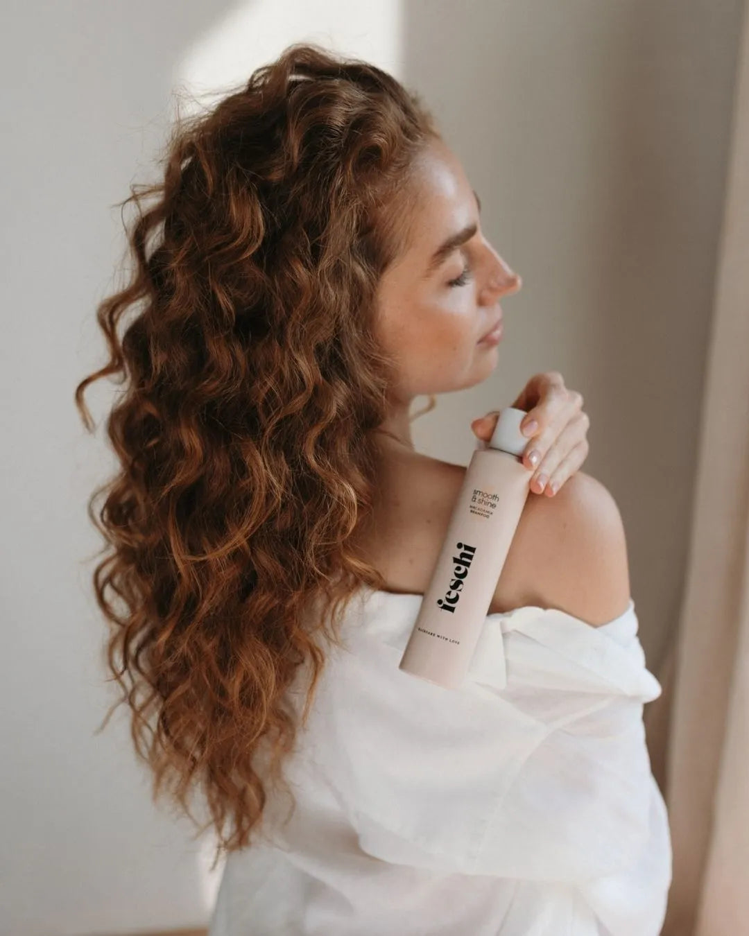 Lockige Frau hält smooth & shine Shampoo über die Schulter