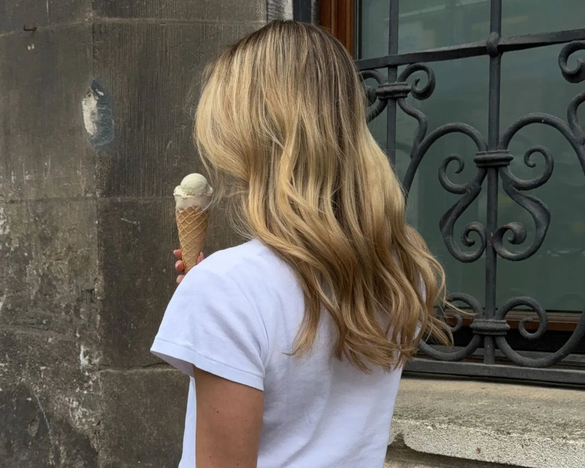 Frau von hinten, stehend vor einem Fenster, hält ein Eis in der Hand