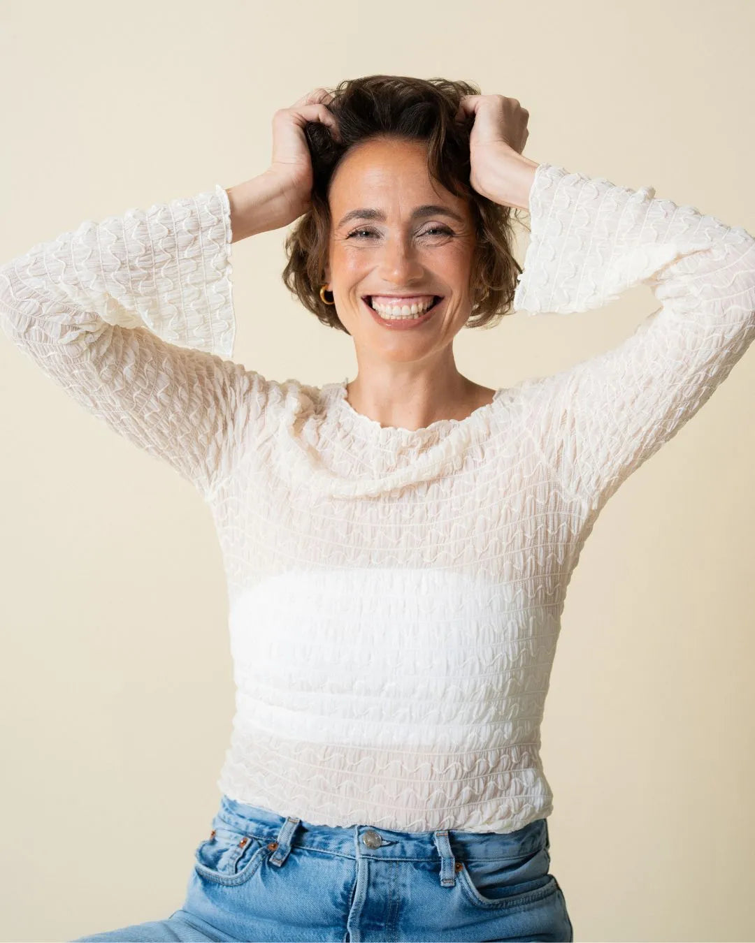 Frau mit kurzen braunen Haaren, lachend, von vorne zu sehen, hält die Hände seitlich an den Kopf