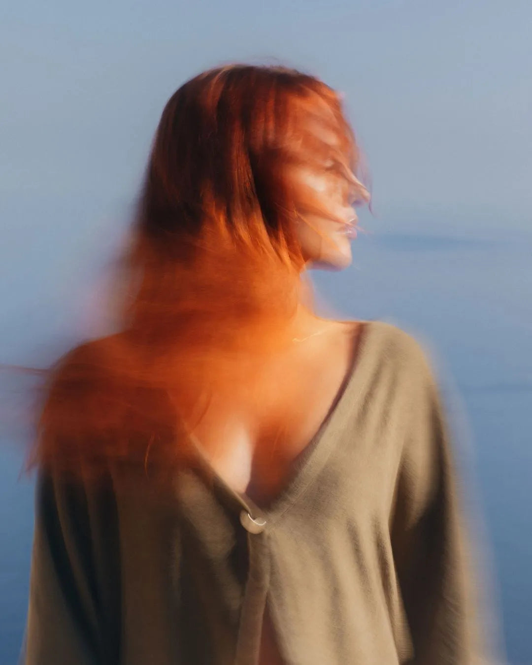 Frau von vorne, blickt seitlich, mit langen roten Haaren, im Hintergrund das Meer