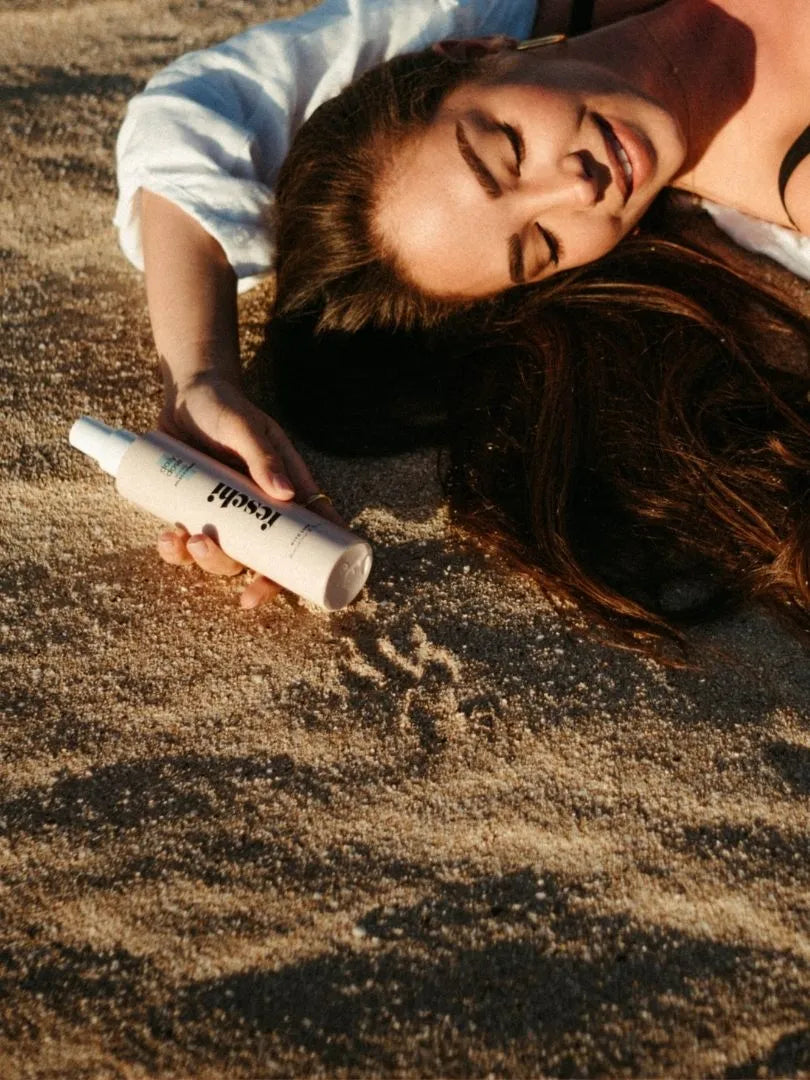Frau liegt am Sand und hält die daily dose Pflegespray Flasche von feschi in der Hand