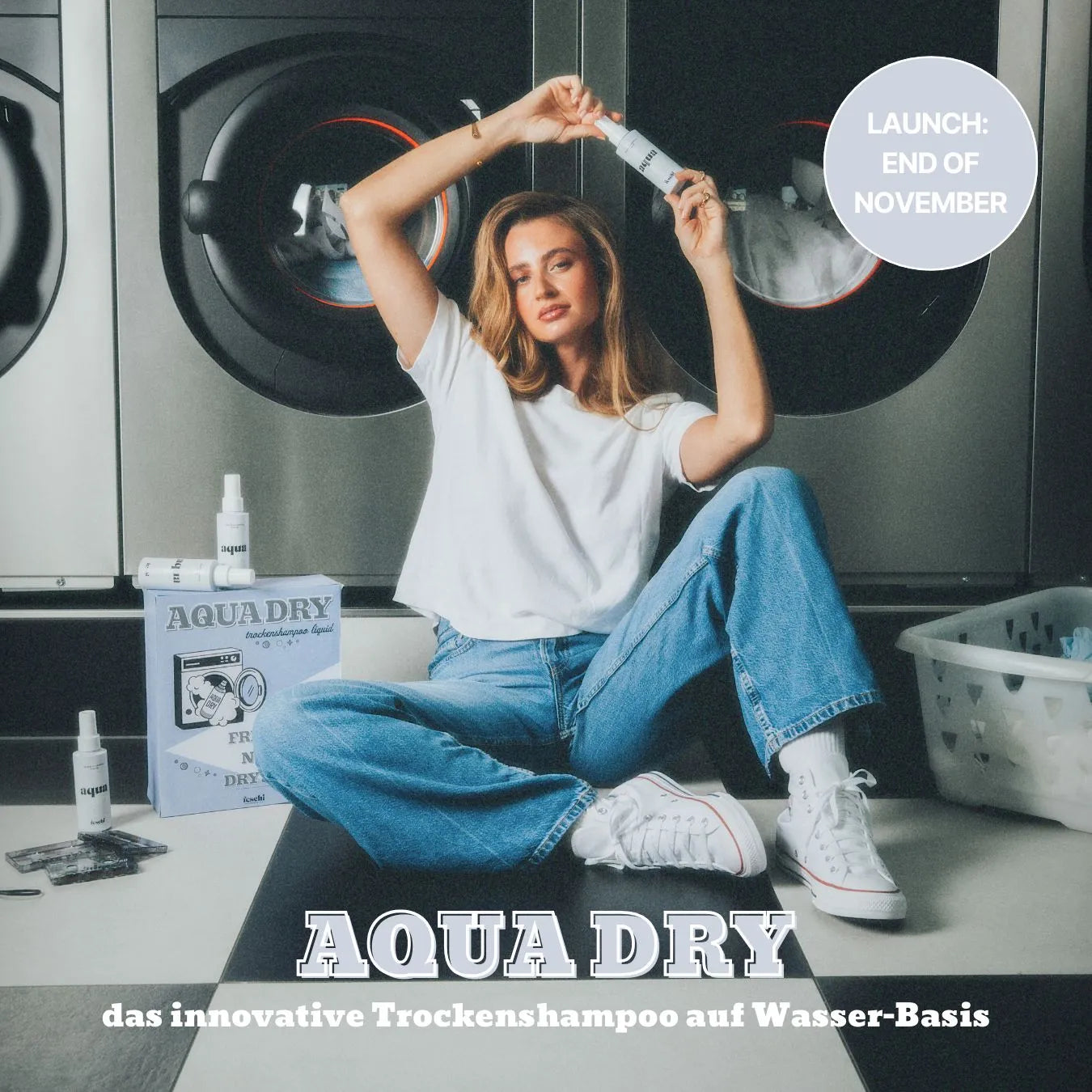 Bild von Frau, die am Boden vor Waschmaschinen sitzt und das neue aqua dry - Trockenshampoo Liquid von feschi in der Hand hält