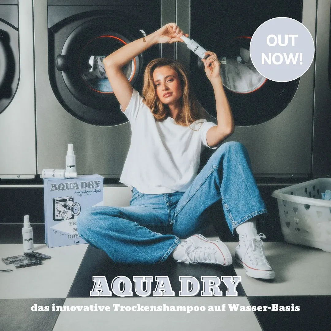 Frau sitzt am Boden vor Waschmaschine und hält das neue feschi Aqua Dry - Trockenshampoo Liquid oberhalb ihres Kopfes.