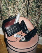 Ein Samthocker mit feschi Stylingprodukten, einer schwarzen Tasche und Pumps