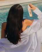 Frau mit langen, glänzenden, braunen Haaren sprüht den feschi daily dose Hydro Pflegespray ins Haar.