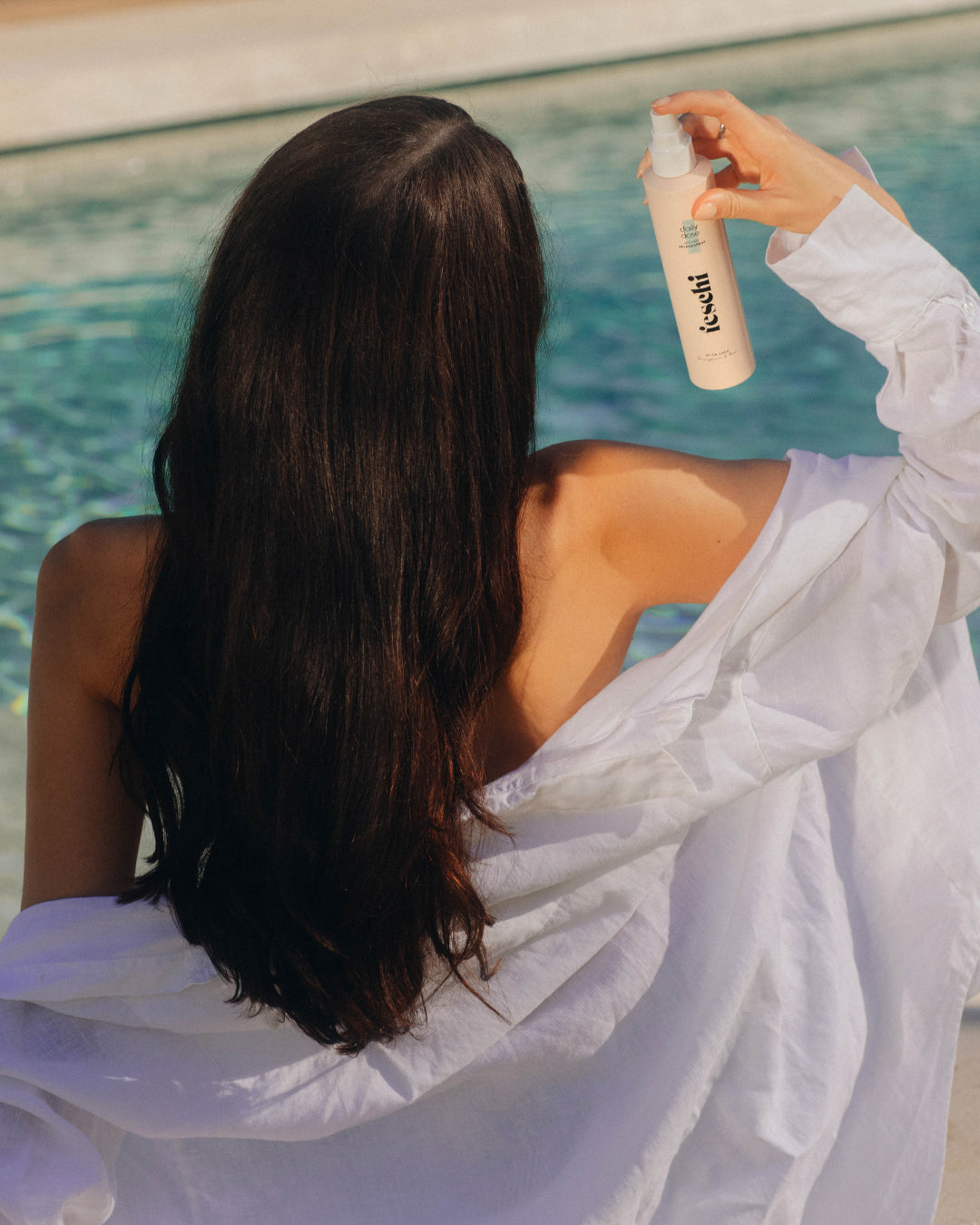 Frau mit langen, glänzenden, braunen Haaren sprüht den feschi daily dose Hydro Pflegespray ins Haar.