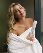 Blonde junge Frau mit sehr voluminösem Haar hält den feschi Schaumfestiger in der Hand